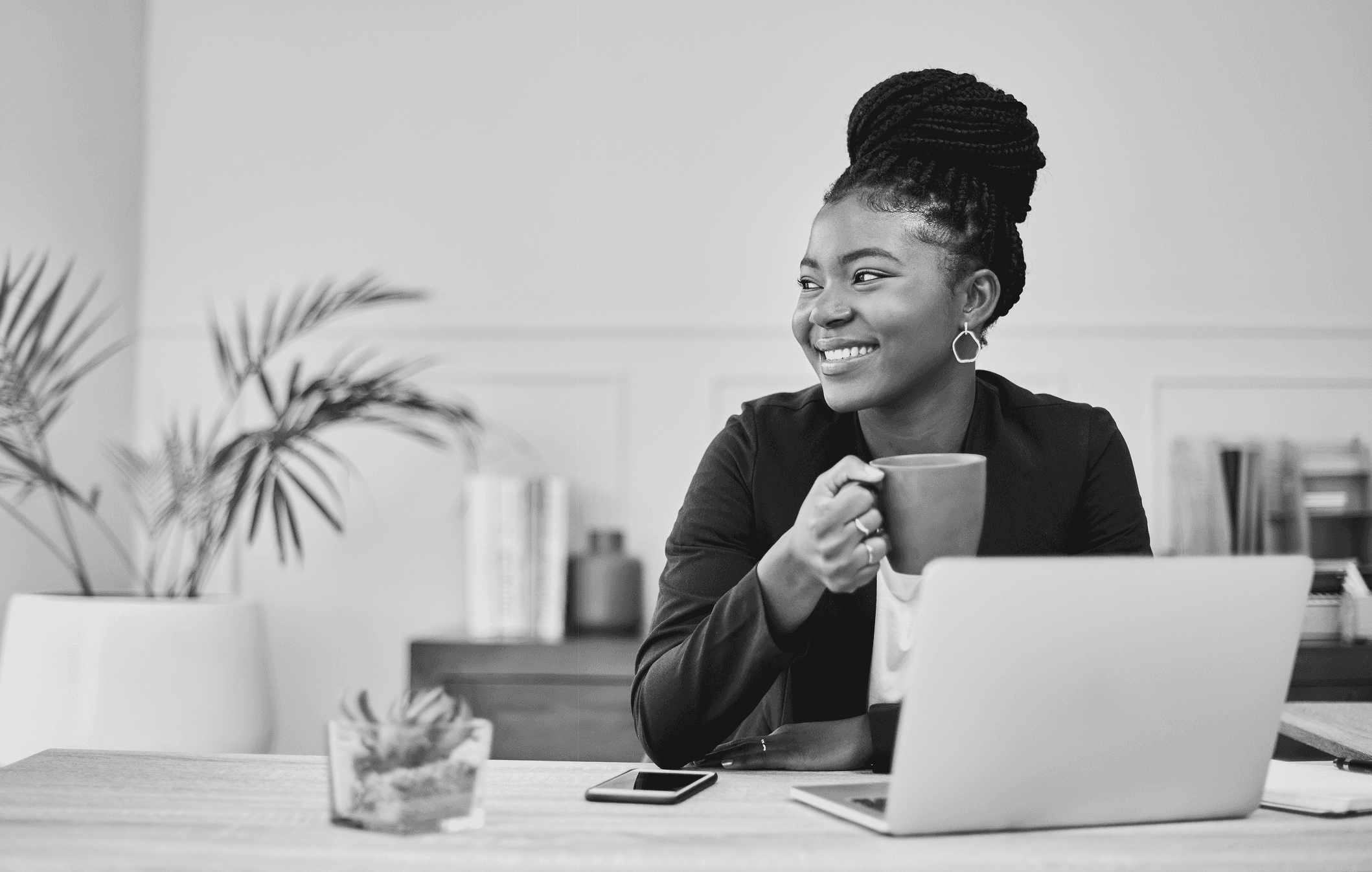 Smart woman holding cup behind a laptop on a desk